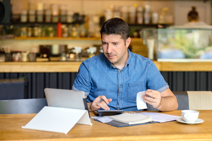 man working on finances while sitting in coffee shop