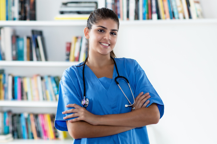 female nurse with stethoscope around her neck standing in front of bookshelves