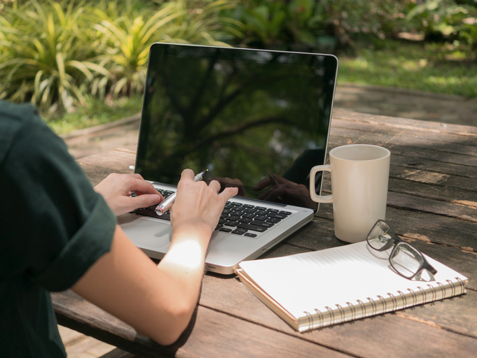 Freelancer working on laptop computer with white coffee cup on the wooden desk in the garden.