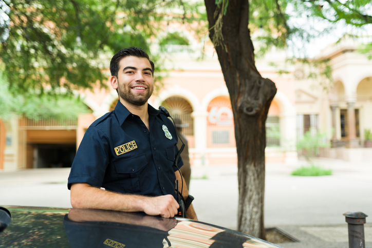 Young man in a police uniform smiling looking at the camera while working as a police officer in the city.