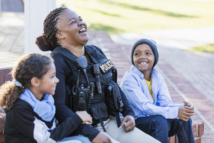 Young police officer laughing while talking to a couple kids.