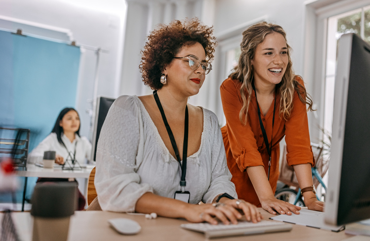 Two business women working on a desktop computer in an office.