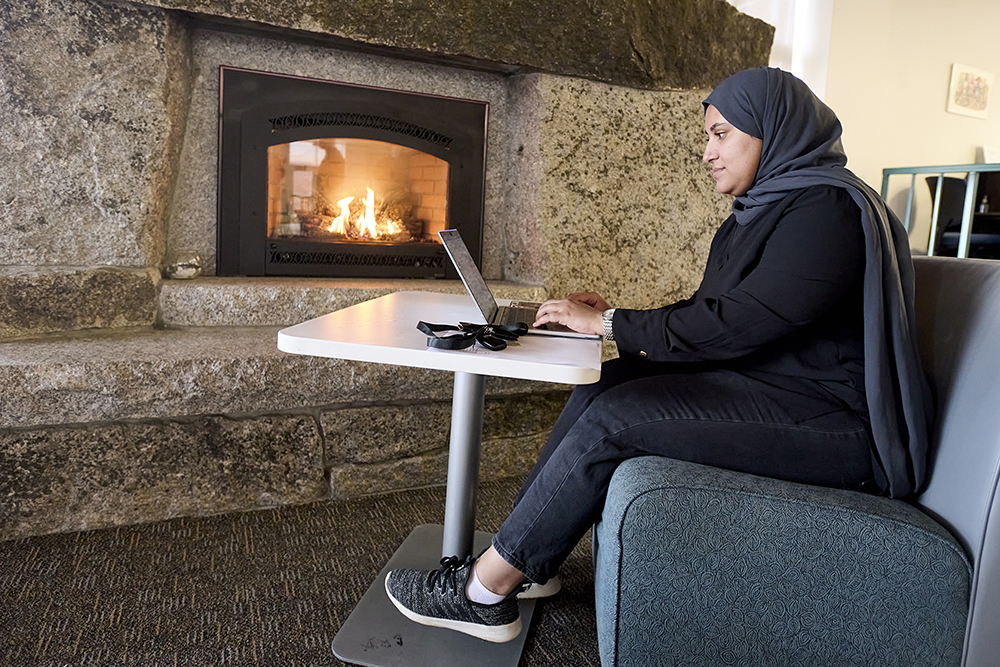 Woman working on a laptop while sitting in front of a fireplace.