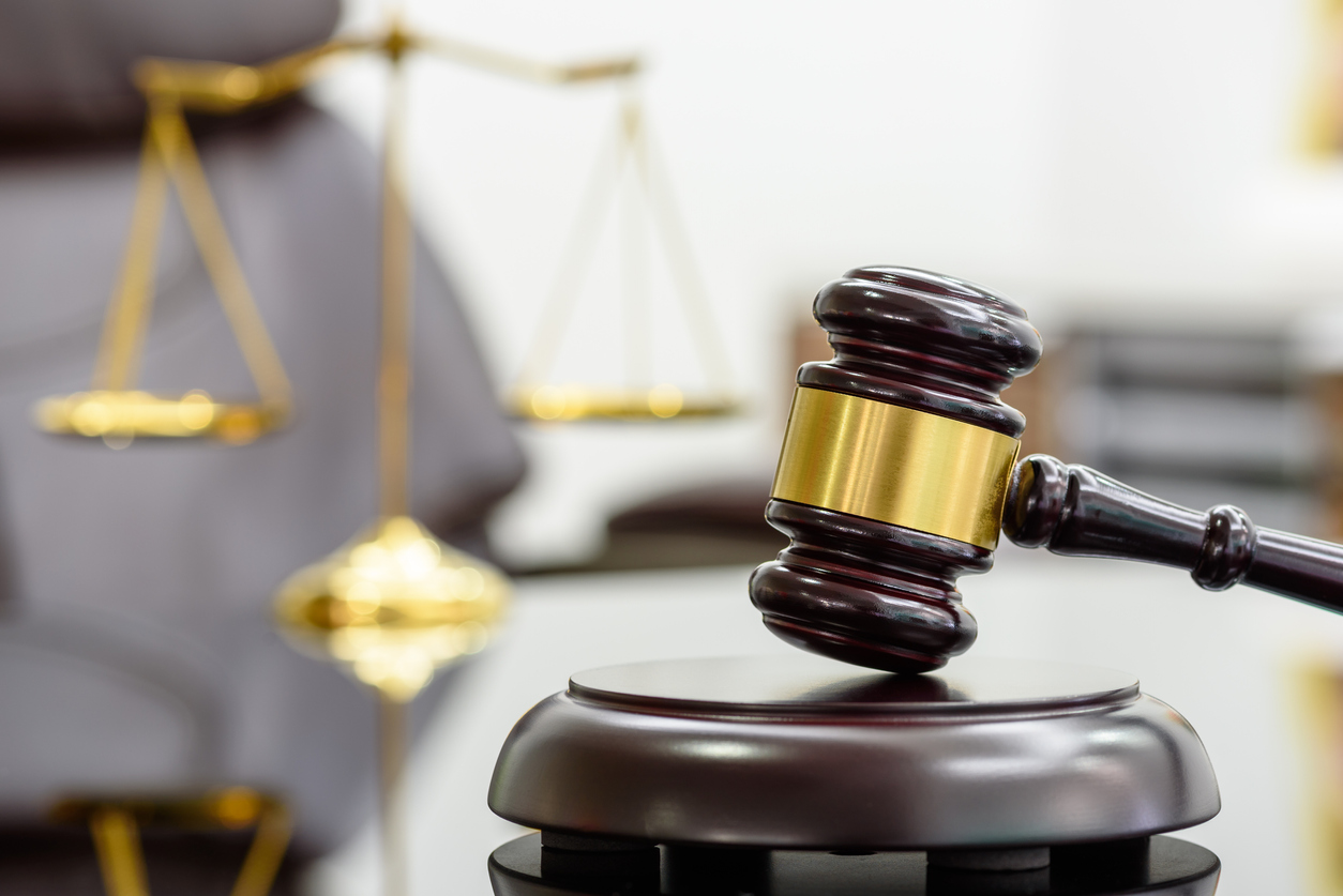 A wood judge gavel resting on a table in front of a brass scale.