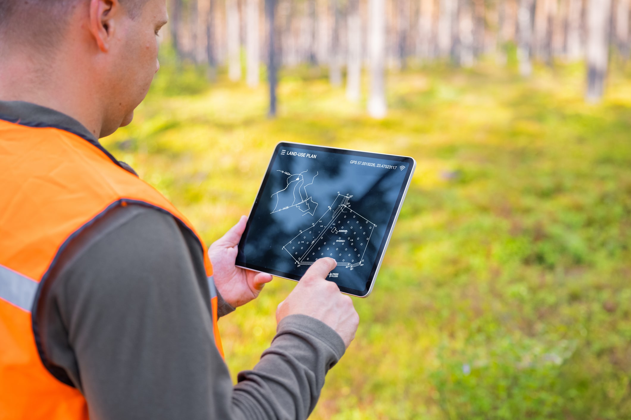 A man who is wearing an orange vest is looking at a topographical map on a tablet computer.