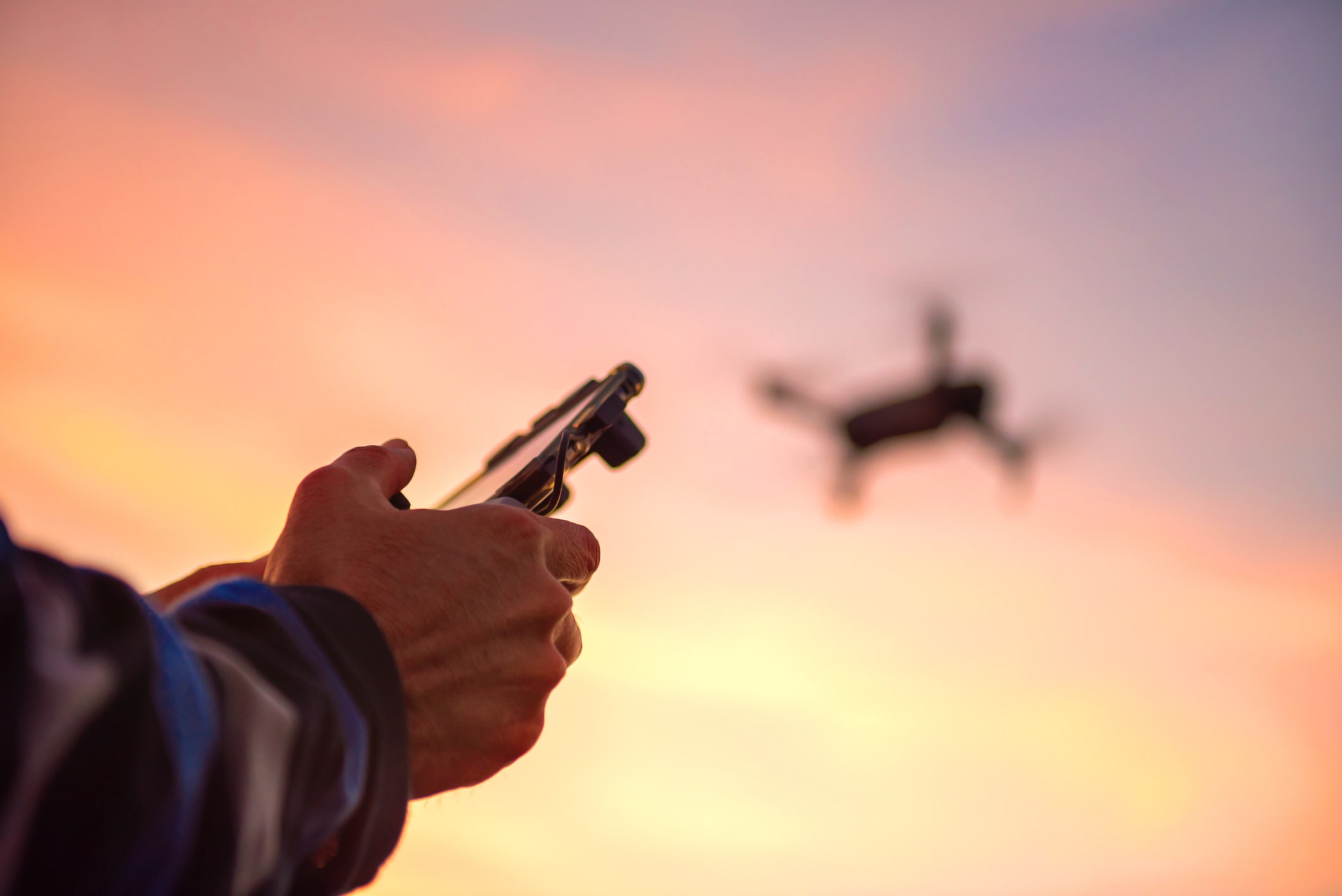 Person operating a drone with a remote control in during sunset.