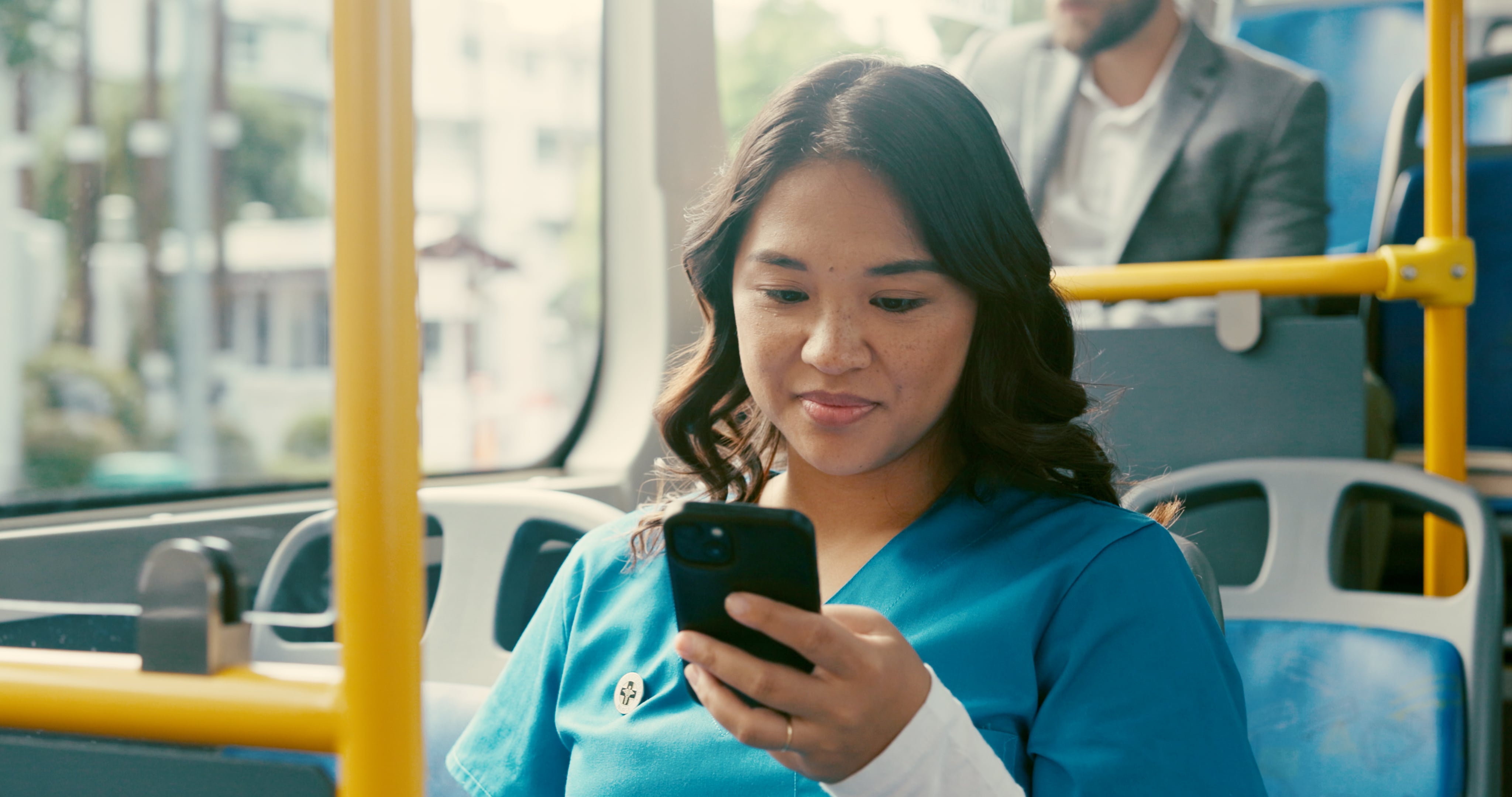 A nurse looking at her phone while riding on a bus.