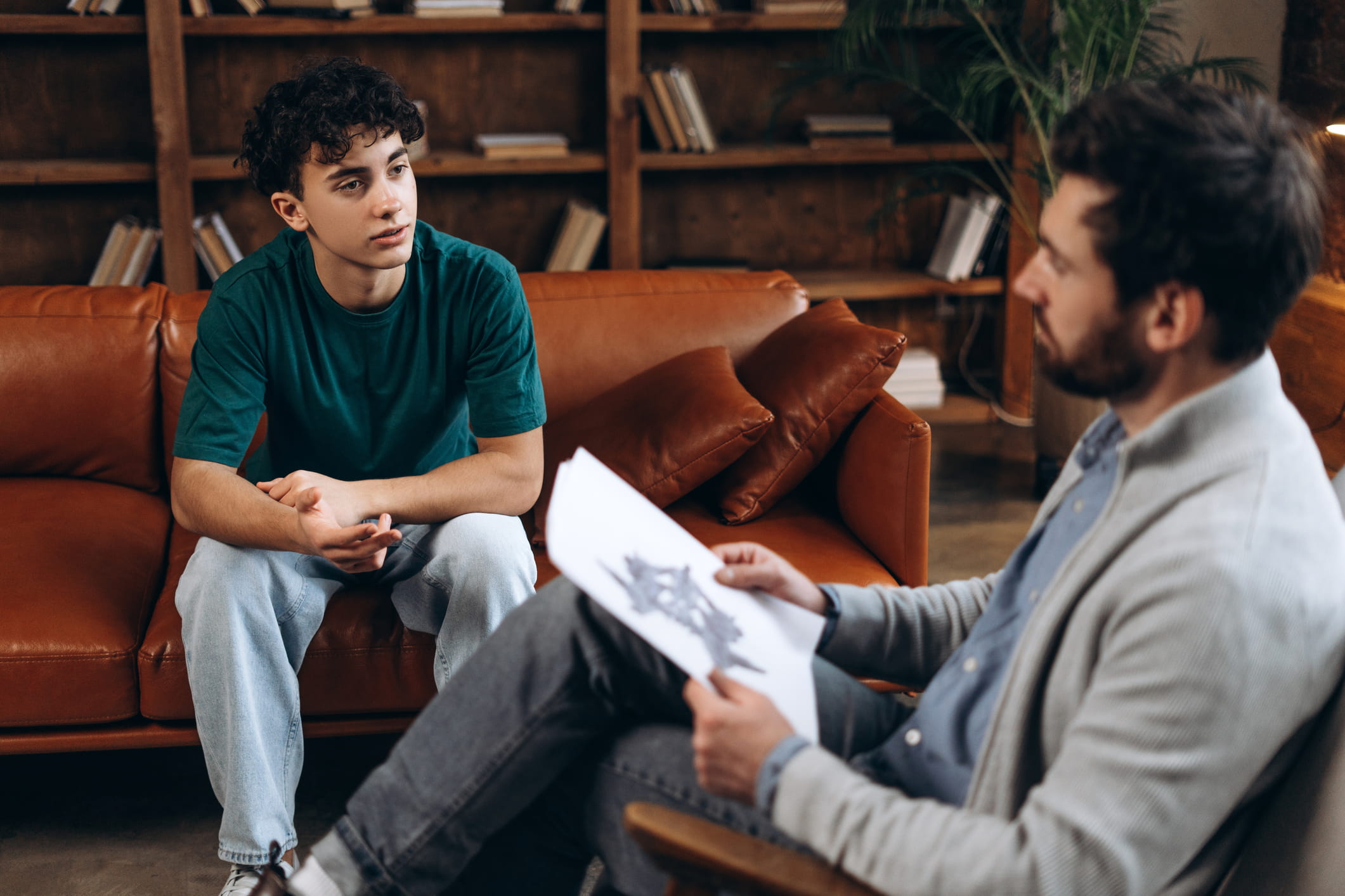 Male therapist talking with teenage boy during counseling session.