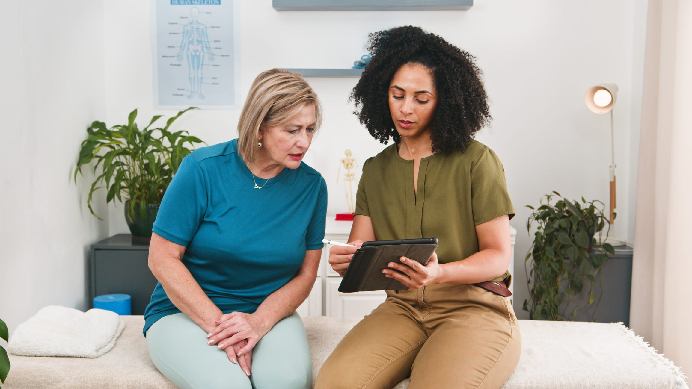 A female physical therapist speaks with a patient while holding a tablet.