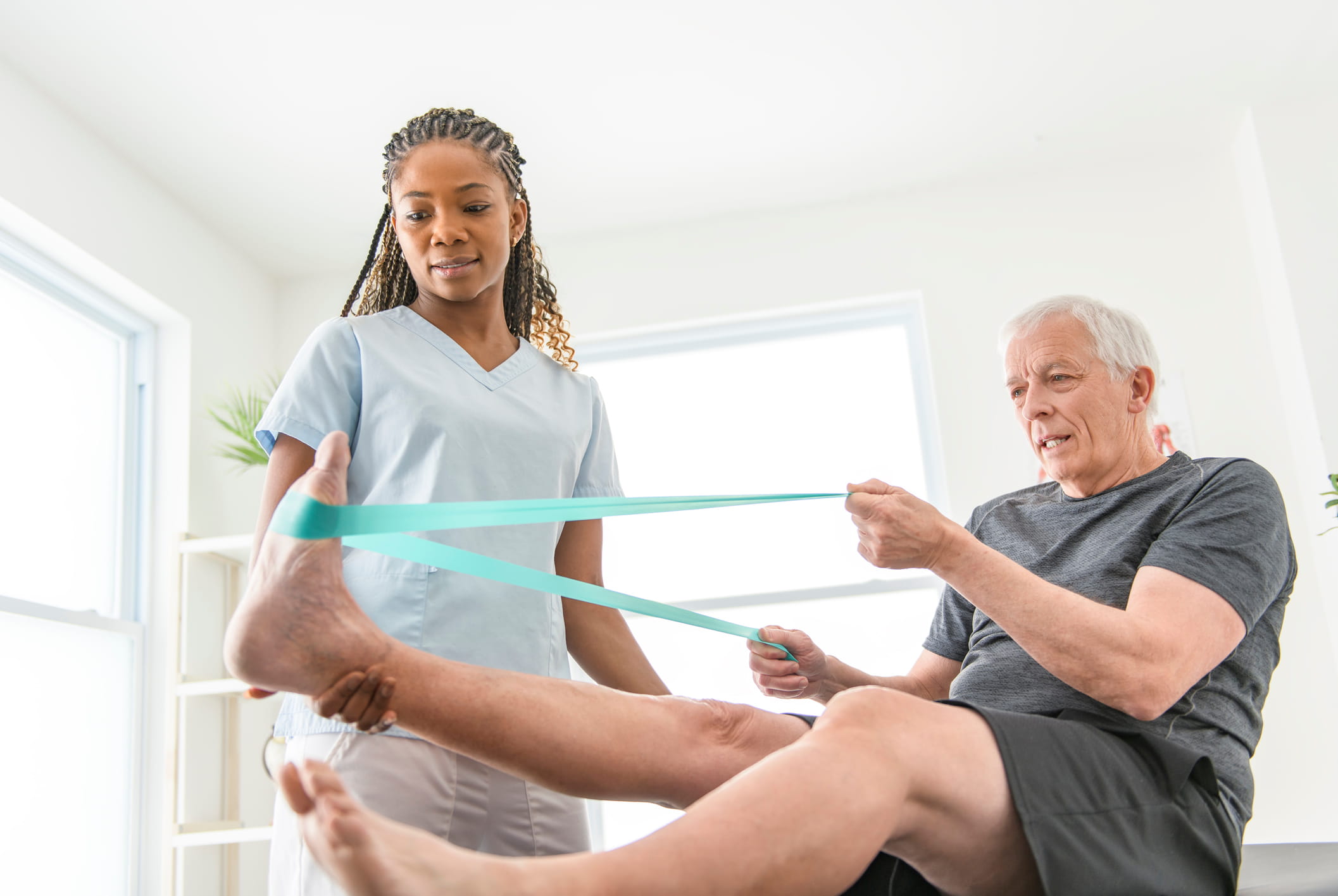 Healthcare professional helps senior male with exercise.