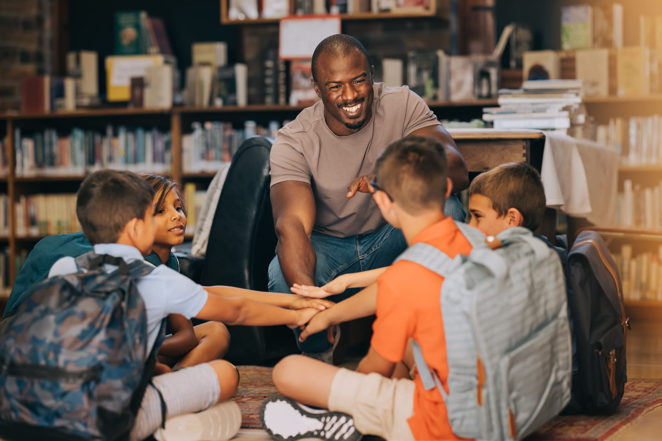 A male education professional huddling with students in a library.